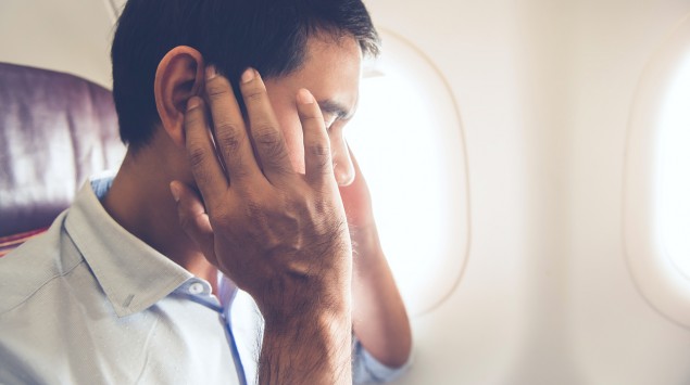 Druck auf den Ohren: Einen Mann sitzt im Flugzeug und drückt die Hände auf seine Ohren.