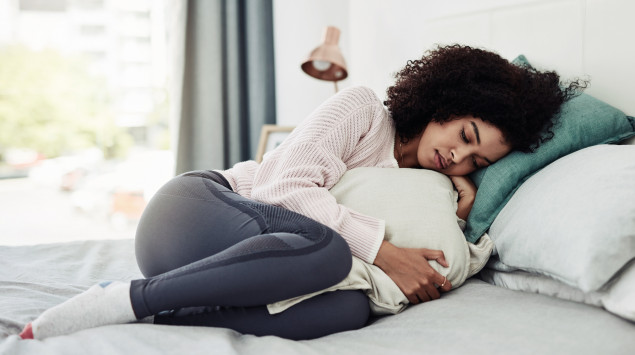 Eine Frau mit Bauchschmerzen liegt im Bett.
