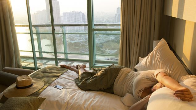 Eine Frau liegt bekleidet auf einem Bett im Hotelzimmer.