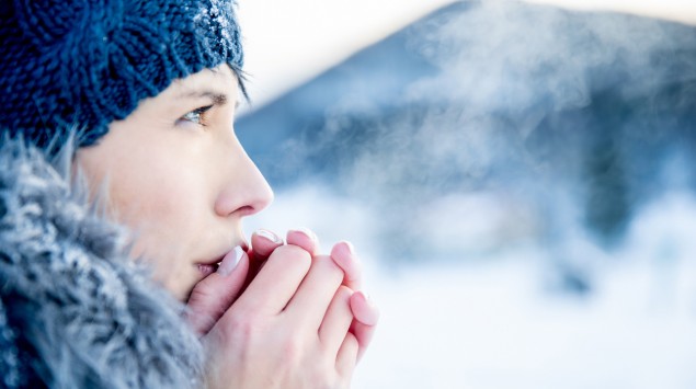 Eine winterlich gekleidete Frau wärmt ihre Hände durch Anhauchen.