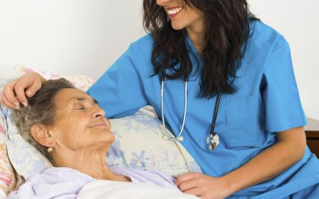 Man sieht eine ältere Frau im Bett und eine Krankenschwester.