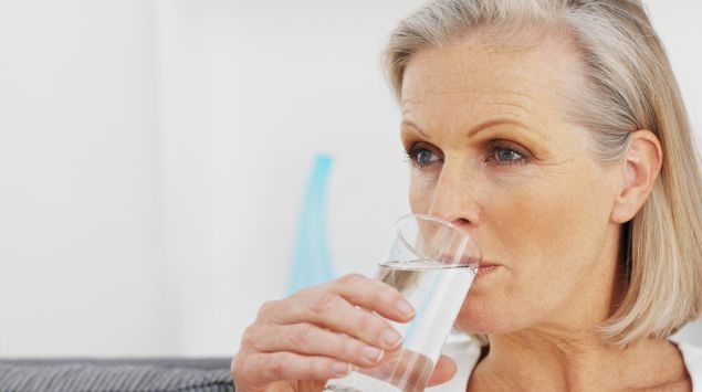 Eine ältere Frau trinkt aus einem Glas Wasser.