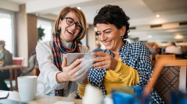 Zwei Frauen schauen sich im Café Bilder am Handy an
