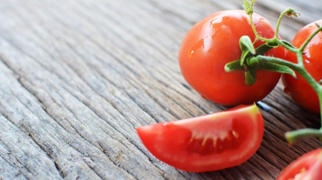 Neben ein paar ganze Tomaten liegen geschnittene Tomatenstücke mit grünem Stielansatz.