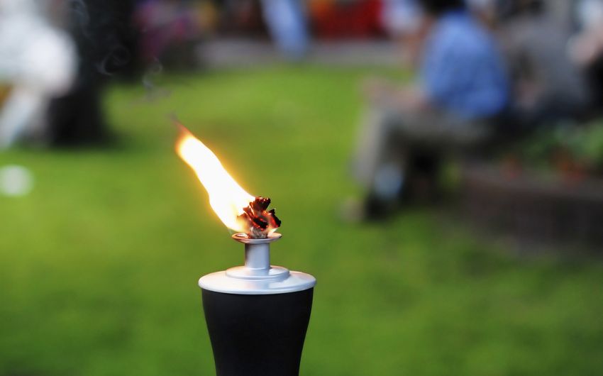 Gesund grillen: Man sieht eine Gartenfackel und Hintergrund ein paar Menschen.