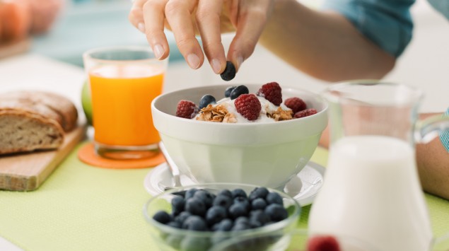 Eine Frau bereitet ein Frühstück mit Müsli und Obst vor.