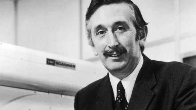 Sir Godfrey Newbold Hounsfield steht vor einem Ct-Gerät.