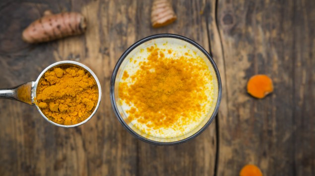 Das Bild zeigt eine Glas mit "Goldener Milch" und einem Löffel mit Kurkuma.