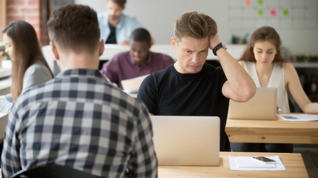 Man sieht ein Großraumbüro mit mehreren Menschen.