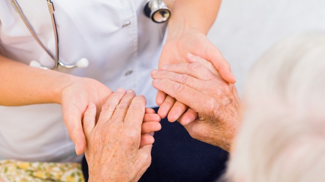 Eine Ärztin hält die Hände eines Seniors.