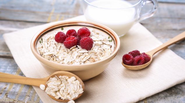 Man sieht eine Schüssel Haferflocken mit Himbeeren und eine Tasse Milch.