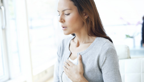 Eine junge Frau legt die linke Hand flach auf die Brustmitte.