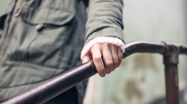 Eine Frau umfasst ein Treppengeländer mit der linken Hand.