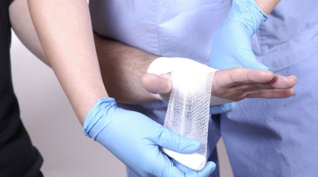 Einem Patienten wird die linke Hand bandagiert.