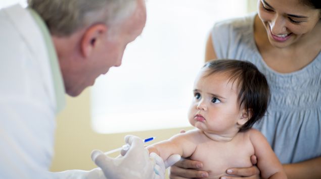 Ein Baby schaut den Arzt während der Impfung an.