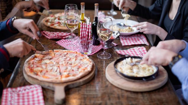 Man sieht einen Tisch in einem italienischen Restaurant, auf dem Pizza- und Pasta-Gerichte stehen.
