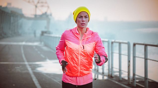 Eine Frau mit einer gelben Mütze joggt über eine Straße.