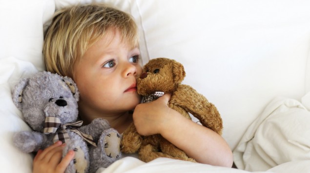 Ein kleiner Junge liegt im Bett und hält in jedem Arm einen Teddybären.