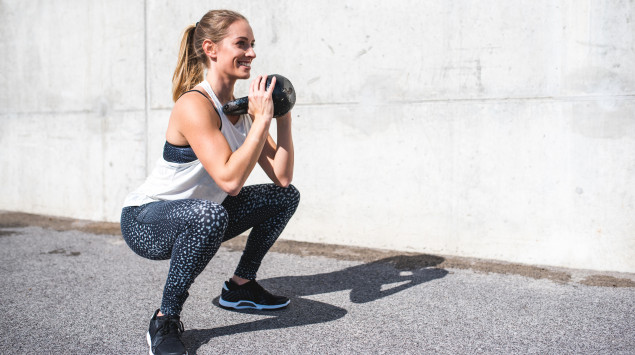 Eine Frau trainiert draußen mit einer Kettlebell.
