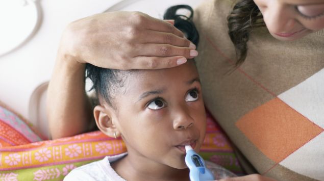 Man sieht eine Mutter, die bei ihrer Tochter Fieber misst.