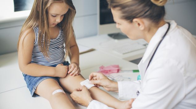 Ein kleines Mädchen bekommt ein Pflaster aufs Knie.