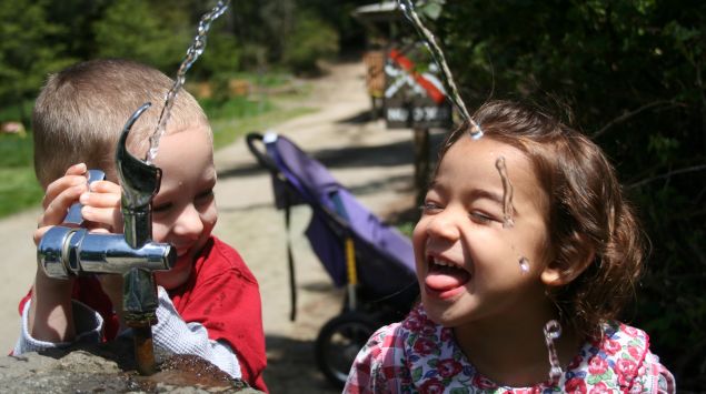 Zwei Kindern trinken an einem Wasserspender.