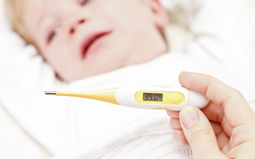 Ein schlagendes Kleinkind im Hintergrund, im Vordergrund ein Fieberthermometer mit dem Wert 39 Grad Celsius