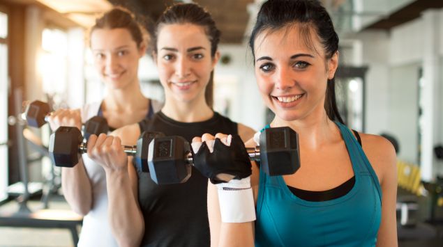 Drei junge Frauen trainieren im Fitnessstudio mit Hanteln