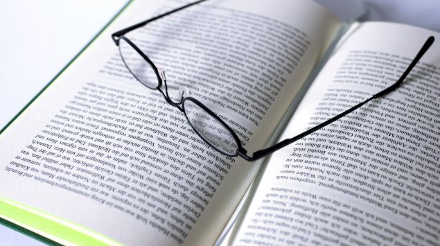 Eine Brille liegt auf einem aufgeschlagenen Buch.