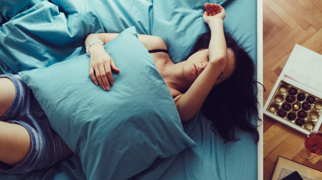 Eine Frau liegt traurig auf dem Bett, neben ihr Wein und Pralinen