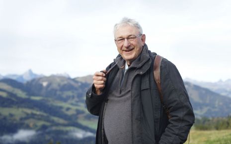 Ein leicht übergewichtiger Mann vor einem Bergpanorama.