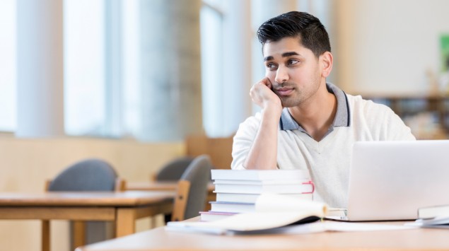 Ein nachdenklich aussehender Mann sitzt am Tisch mit Büchern.