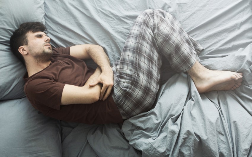 Bauchspeicheldrüsenentzündung: Ein Mann liegt mit starken Bauchschmerzen im Bett und hat eine Schonhaltung mit angezogenen Beinen eingenommen.