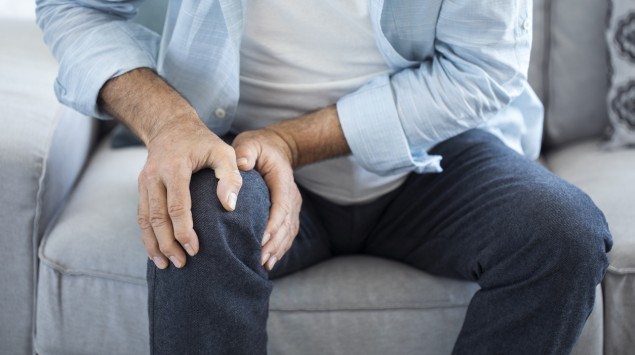 Ein Mann sitzt auf einem Sofa und greift sich ans schmerzende Knie.