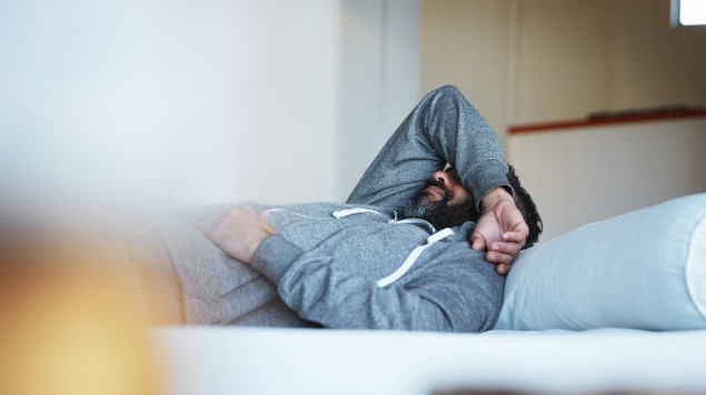 Ein Mann liegt auf dem Bett und hat einen Arm über die Augen gelegt.