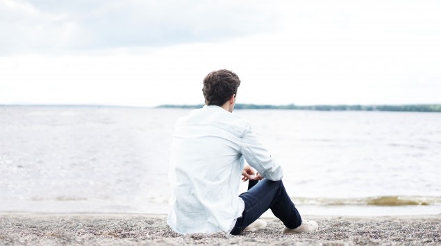 Das Bild zeigt einen jungen Mann, der an einem See sitzt.