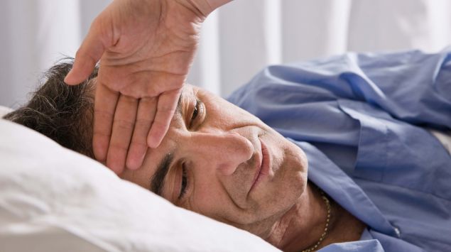 Man sieht einen Mann mit Fieber im Bett.
