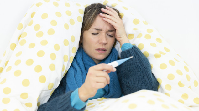 Frau liegt mit Fieber im Bett. Hat sie Covid-19 oder Grippe?