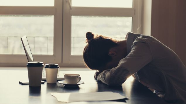 Das Bild zeigt eine Frau, die am Tisch sitzt und ihren Kopf auf den Unterarm stützt