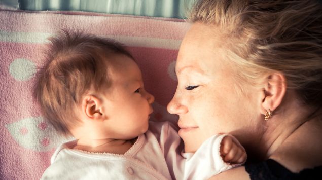 Das Bild zeigt ein neugeborenes Baby, das neben seiner Mutter liegt.