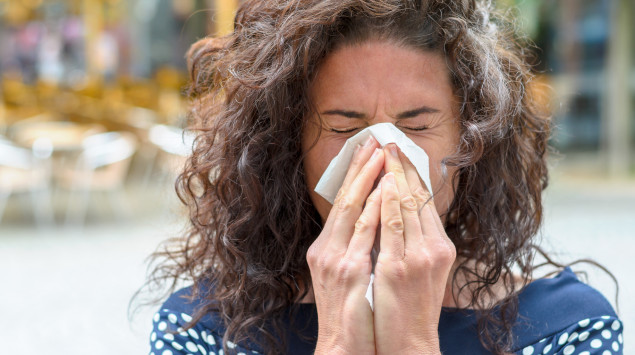 Eine Allergikerin niest in ein Taschentuch. Wie sich die Symptome bei Covid-19 und einer Allergie unterscheiden.