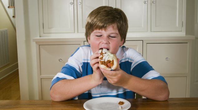 Das Bild zeigt einen übergewichtigen Jungen, der einen Hotdog ist.