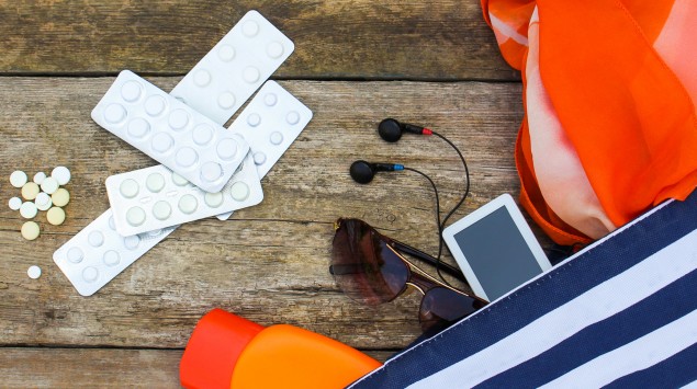 Tabletten aus Reiseapotheke neben Badetasche