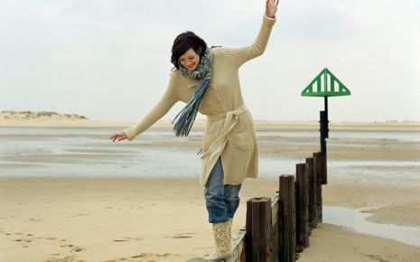 Eine Frau balanciert am Strand auf einem Holzpfosten.