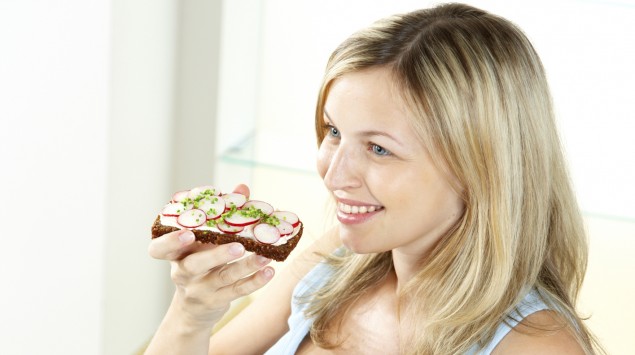 Das BIld zeigt eine junge Frau, die eine Scheibe Vollkornbrot isst.