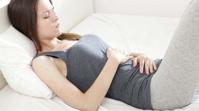 Eine Frau liegt im Bett und hält sich den Bauch.