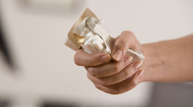 Das Bild zeigt eine Hand, die eine Packung Zigaretten zerdrückt.