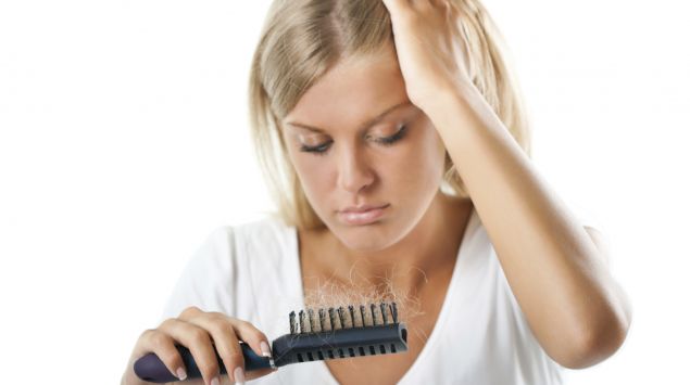 Das Bild zeigt eine Frau, die af die Haare in ihrer Bürste schaut.
