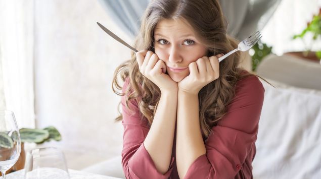 Das Bild zeigt eine Frau am Tisch sitzend mit Messer und Gabel in der Hand.