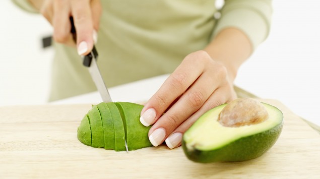 Das Bild zeigt eine Frau, die eine Avocado aufschneidet.